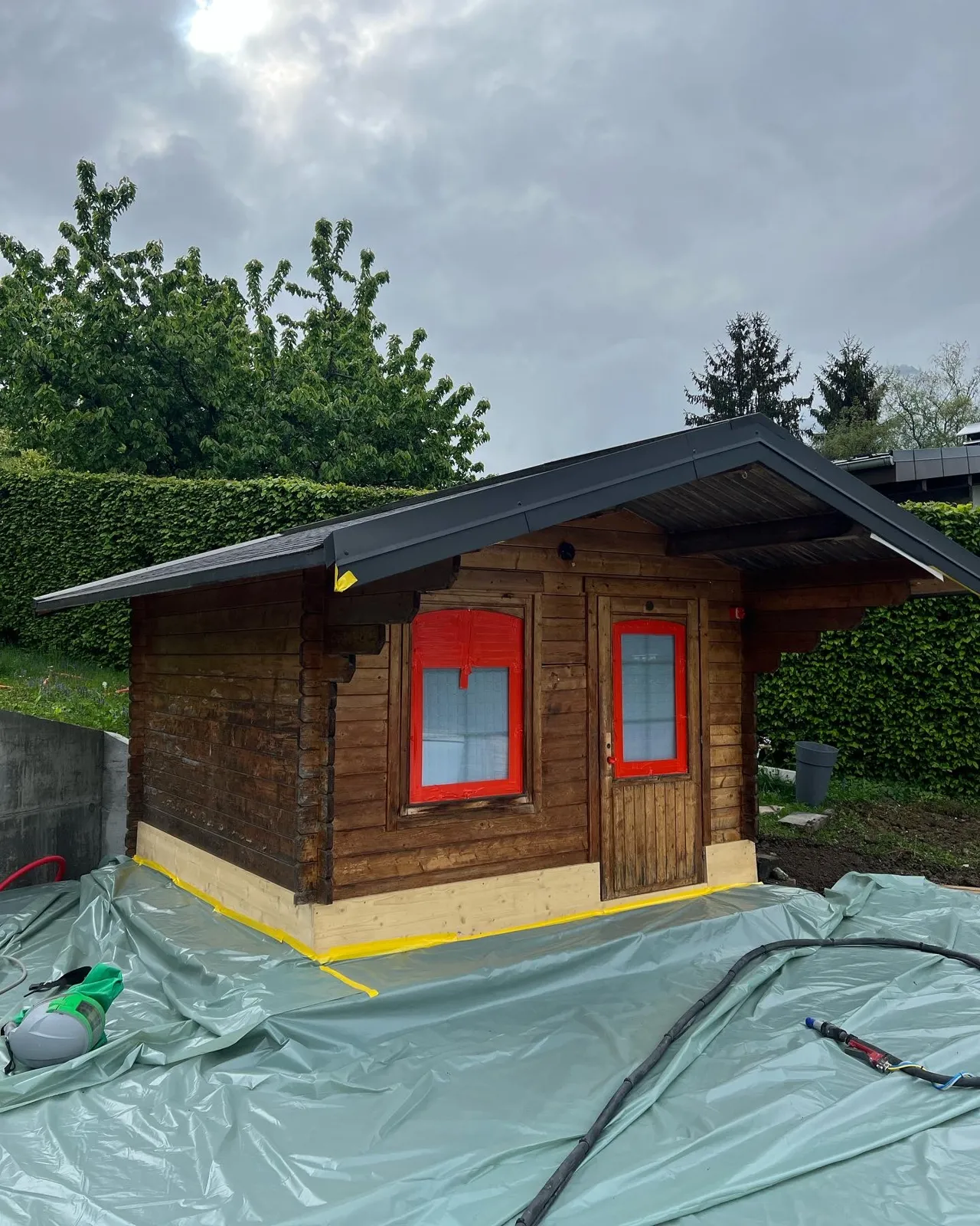 Abri de jardin en bois foncé protégé par bâche avant sablage