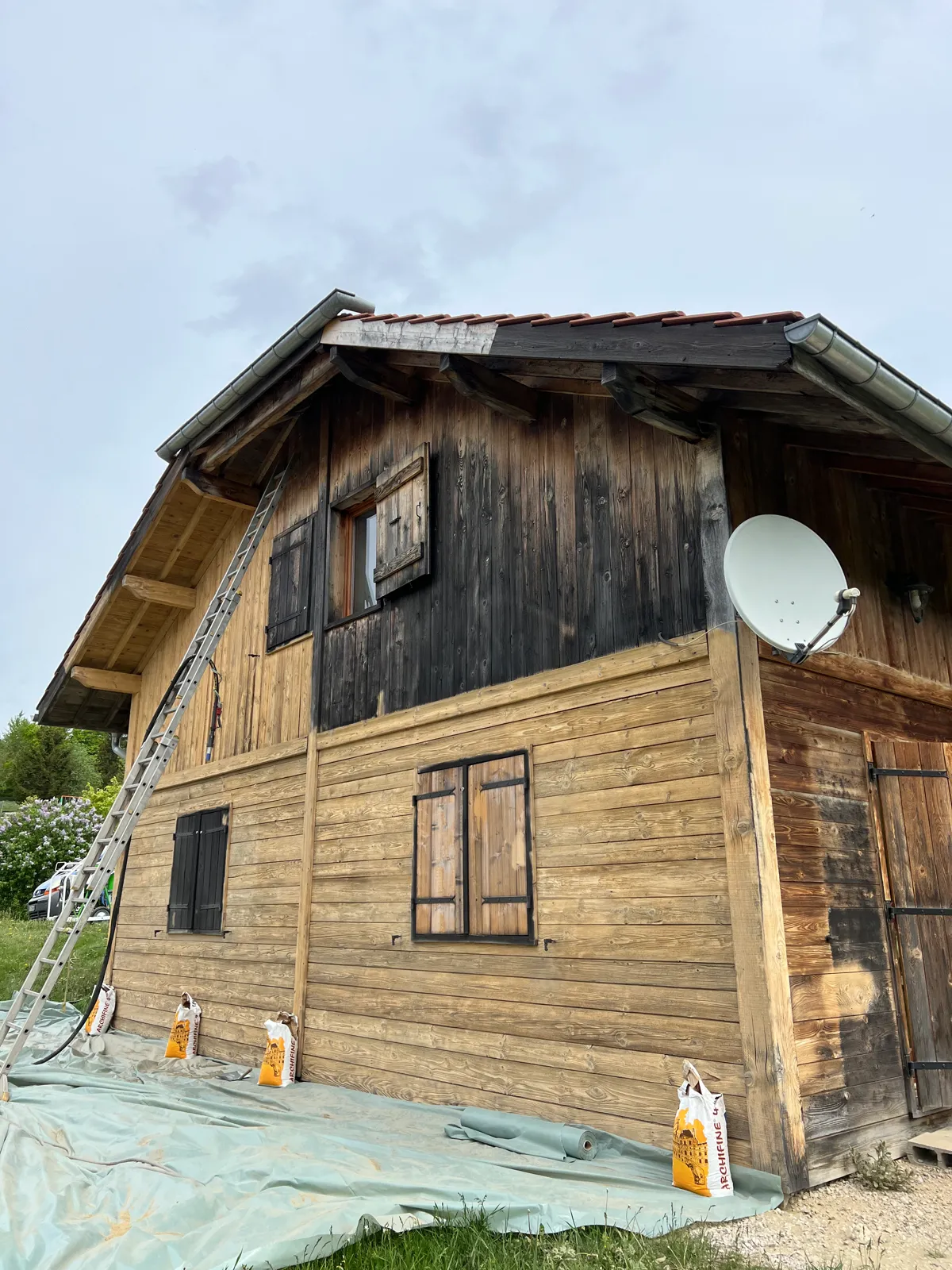 Décapage d'une grange en bois : partie basse déjà sablée, partie haute encore noircie